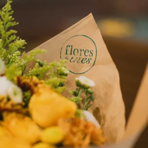 Flores de Ines branded kraft paper wrapping a bouquet of yellow and white flowers with green foliage