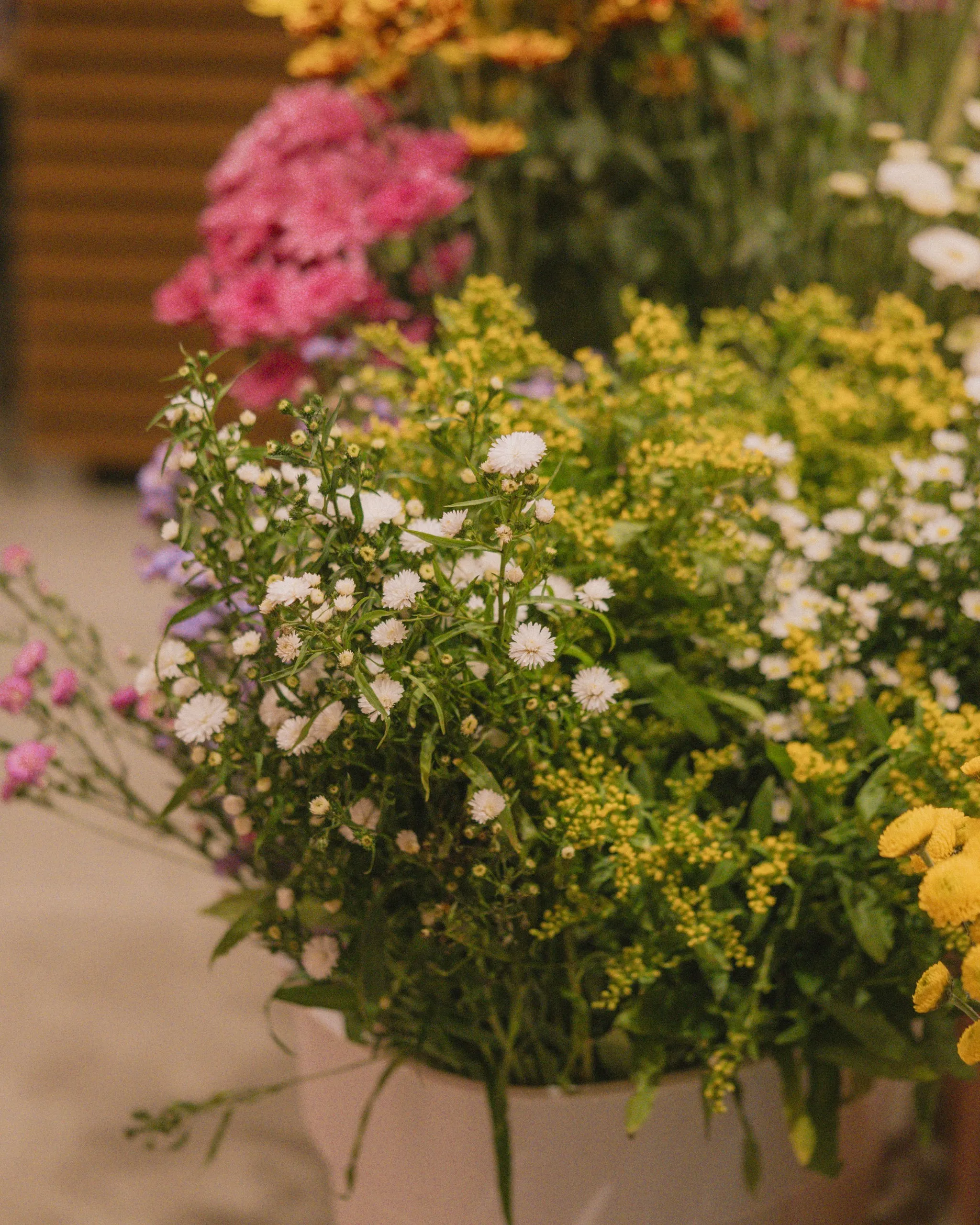Buckets of mixed wildflowers including white asters, yellow goldenrod, and pink blooms displayed at a flower market