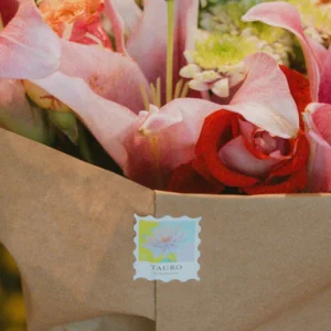 Bouquet of pink calla lilies, red roses, and white flowers wrapped in kraft paper with a Tauro El hedonista branded sticker