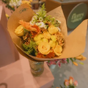 Bouquet of yellow roses, orange gerberas, and mixed flowers wrapped in kraft paper at a flower shop